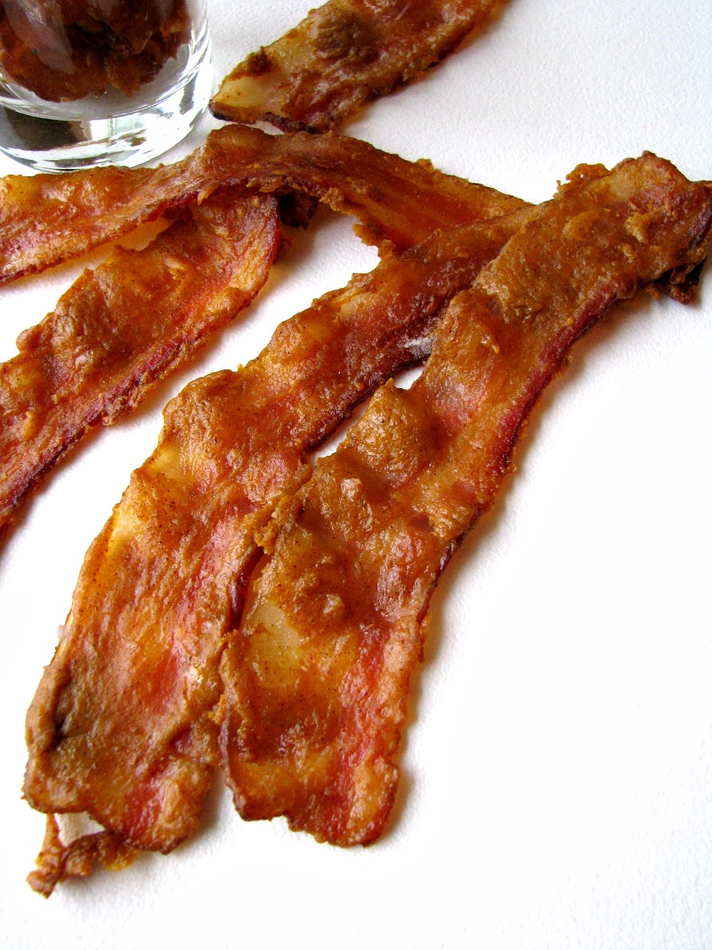Photo of bacon on a white board with several slices of bacon in a cup