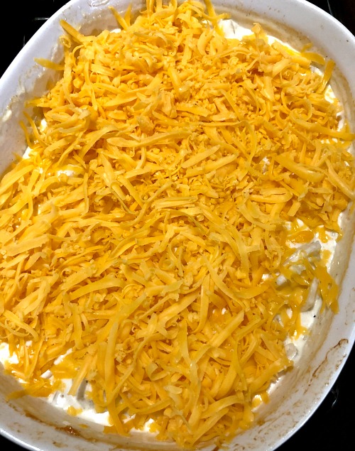 photo of potatoes topped with shredded yellow cheddar cheese in a baking dish 