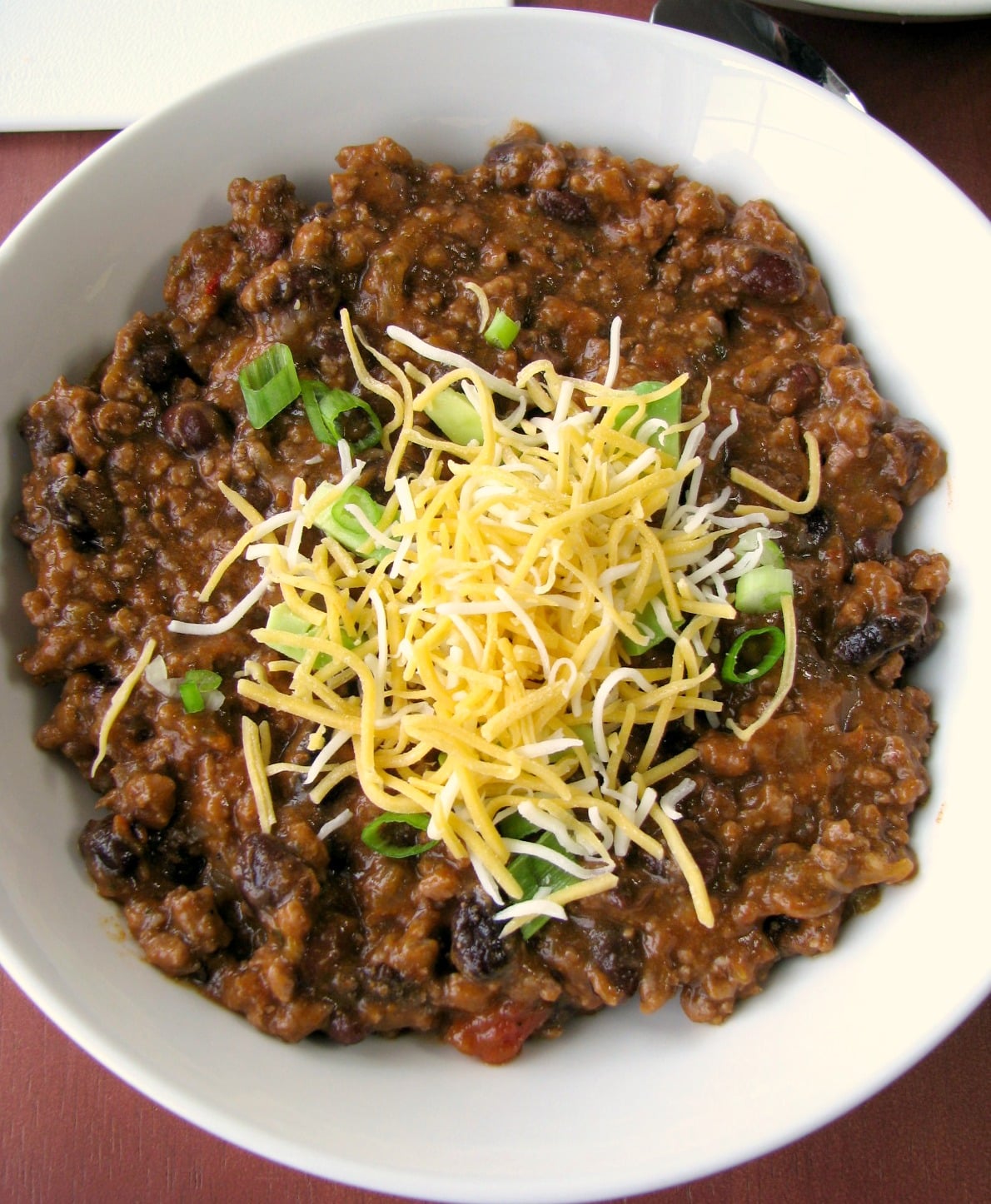 Close up photo of 5 Ingredient Taco Soup in a white bowl topped with shredded cheese and scallions