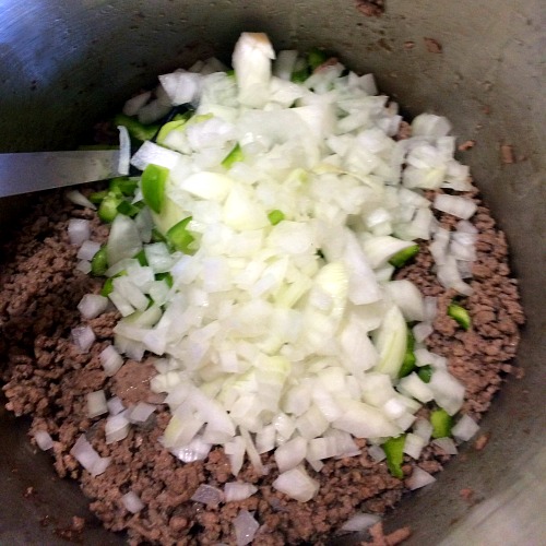 Photo of cooked ground beef topped with chopped onions and green peppers in a large pot