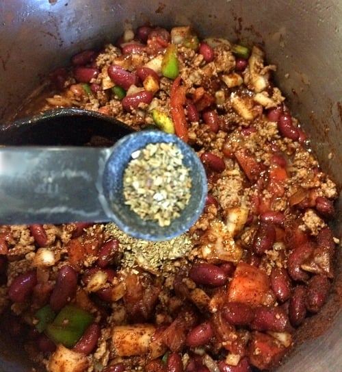 photo of dried basil being added to a large pot of chili 