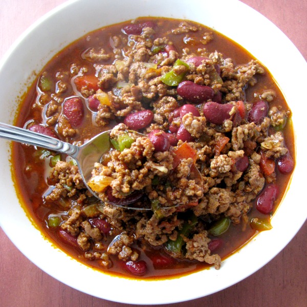 Photo of Award Winning Chili in a white bowl on a wood table with a raised spoonful of chili 
