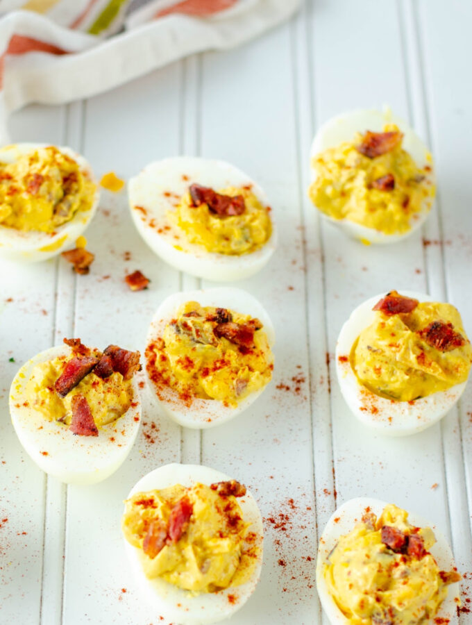 bacon cheddar deviled eggs on a white wooden board with bacon crumbles and paprika sprinkled around for decoration