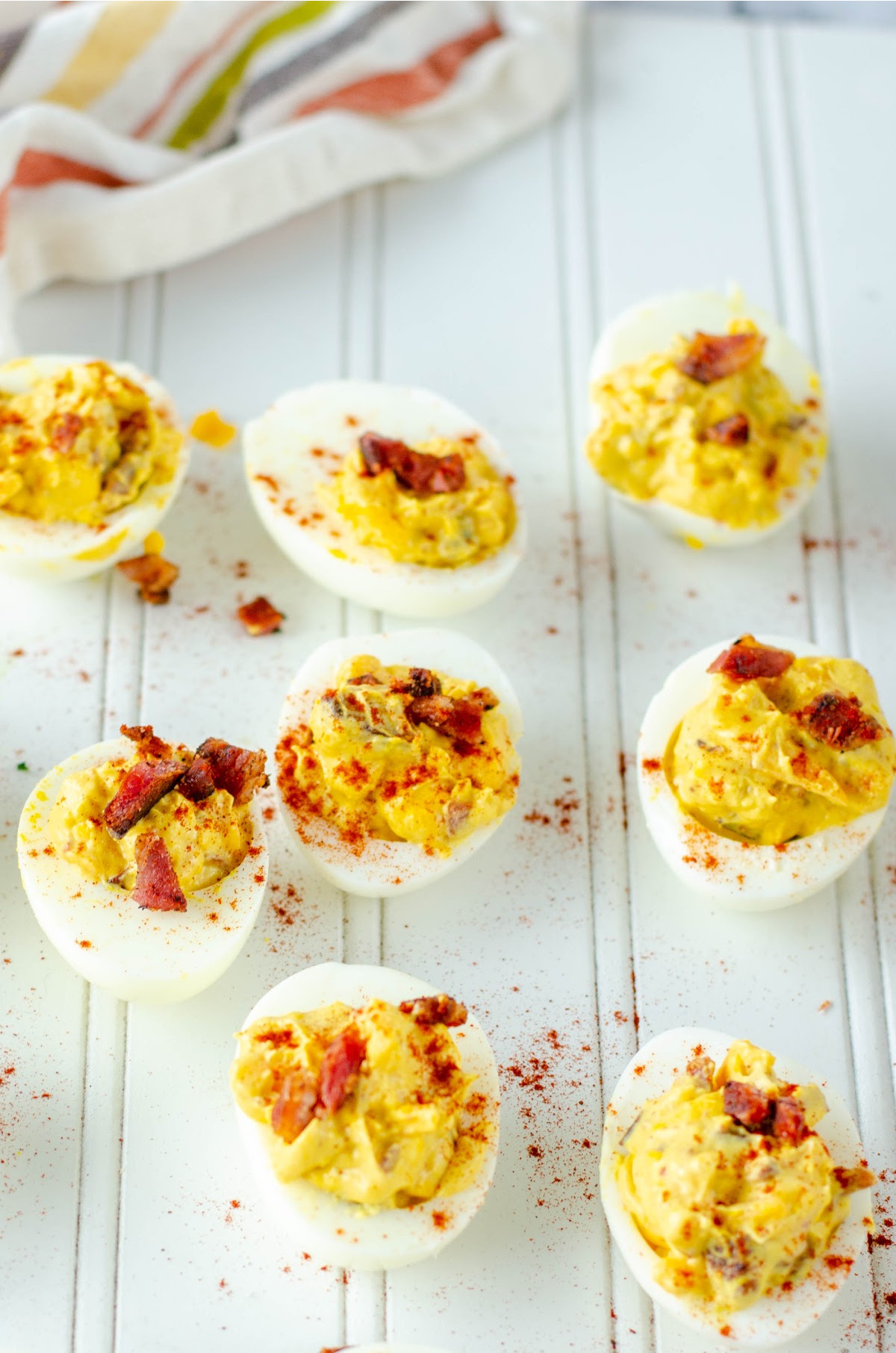 bacon cheddar deviled eggs on a white wooden board with bacon crumbles and paprika sprinkled around for decoration 