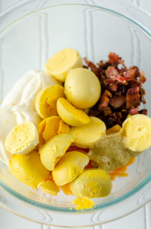 eggs yolks in a glass bowl with crumbled bacon mayonnaise and mustard 