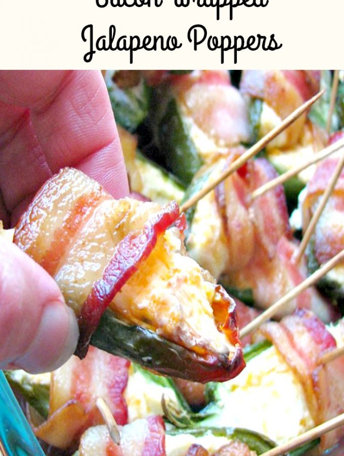 Close up photo of a hand holding a Bacon Wrapped Jalapeno Popper with a pan of poppers in the background
