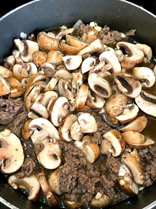 photo of sliced mushrooms and garlic added to cooked ground beef 