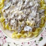 photo of Easy Beef Stroganoff over egg noodles on a white plate with flower trim