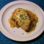 Photo of plated Chicken Parmesan over thin spaghetti on a white plate with a blue place mat