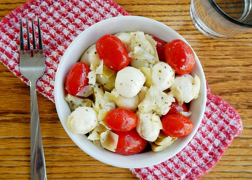 Overhead photo of Mozzarella Tomato Artichoke Salad in a white bowl on a red checkered napkin