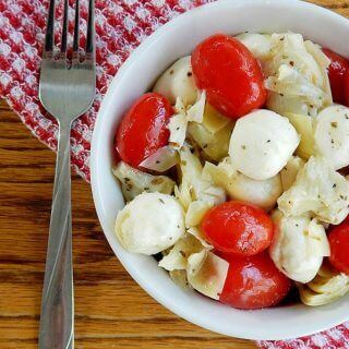 Photo of a white bowl on top of a checkered red napkin filled with Mozzarella Tomato Artichoke Salad