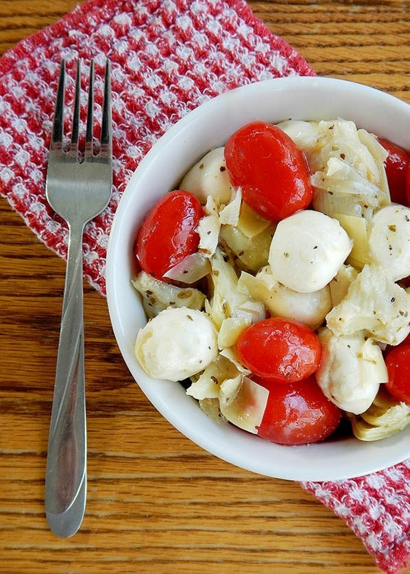 Photo of a white bowl on top of a checkered red napkin filled with Mozzarella Tomato Artichoke Salad