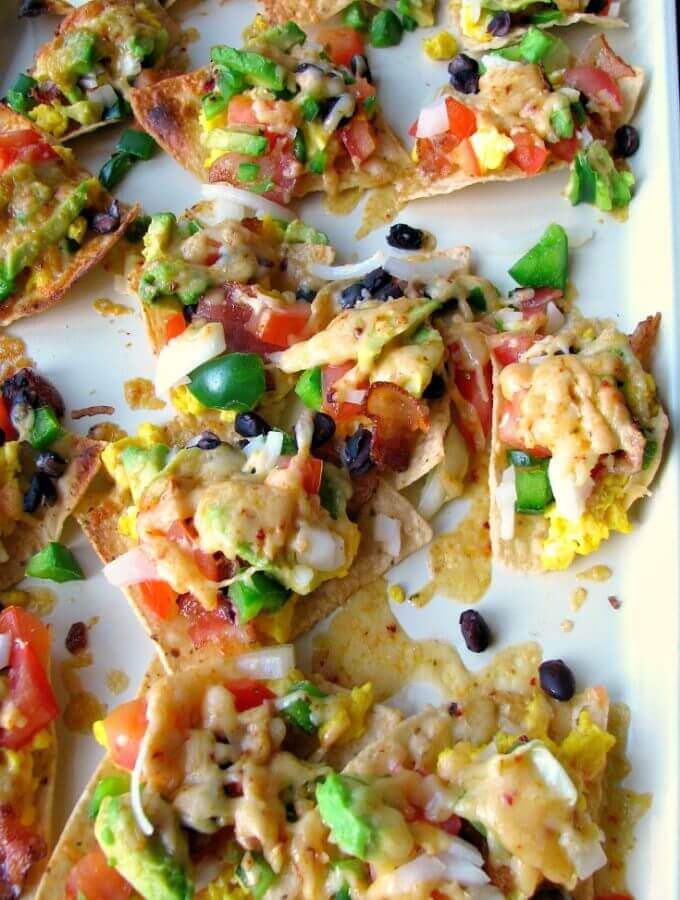 These Cheesy Breakfast Nachos are topped with scrambled eggs, bacon, tomatoes, bell peppers, onions, chipotle cheddar, and black beans.