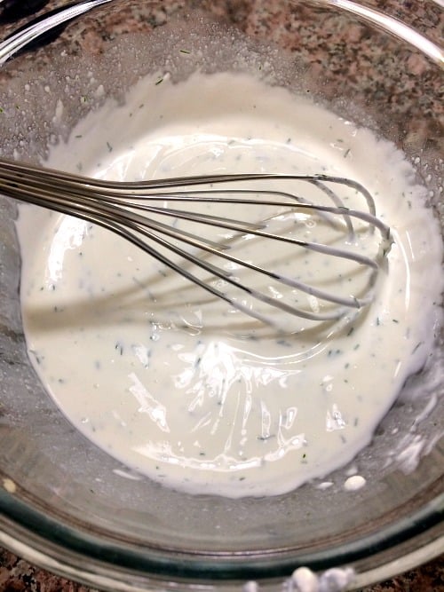photo of mixed sour cream vinegar and dill in a glass bowl with a metal whisk