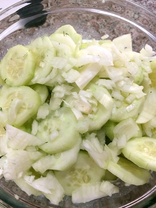 Photo of sliced cucumbers and onions over sour cream and vinegar mixture in a glass bowl 