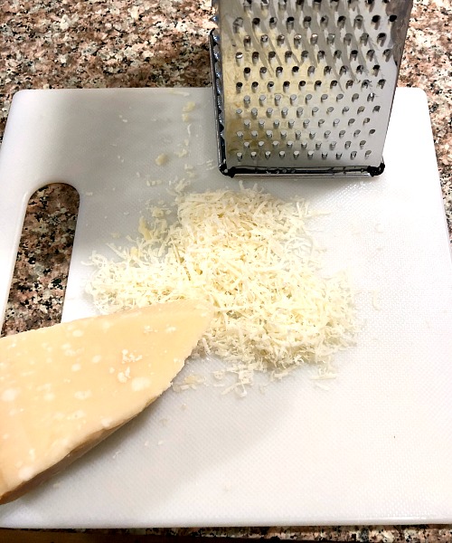 photo of shredded Parmigiano reggiano on a cutting board next to a box grater 