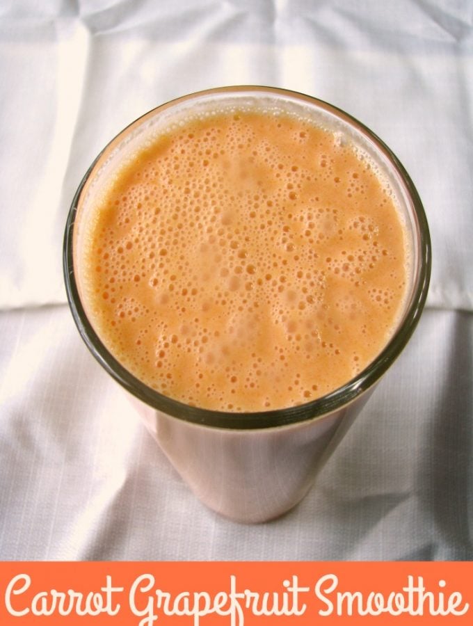 Overhead photo of Carrot Grapefruit Smoothie a light orange drink in a clear glass set on a white tablecloth