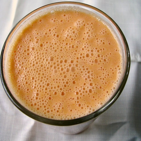 Square overhead photo of orange Carrot Grapefruit Smoothie in a clear glass on a white tablecloth 