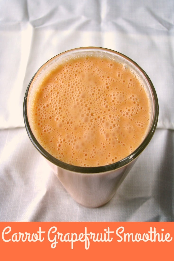Overhead photo of Carrot Grapefruit Smoothie a light orange drink in a clear glass set on a white tablecloth 