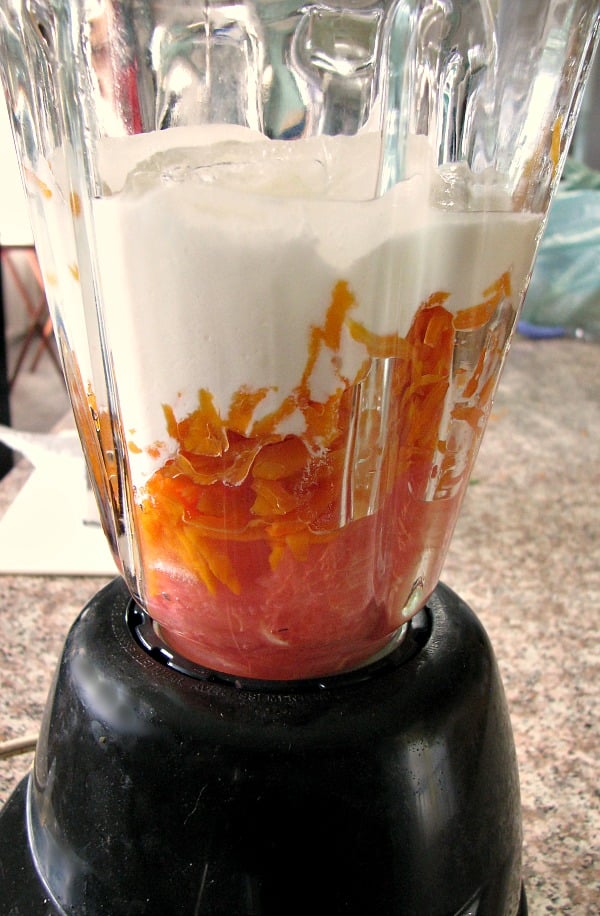 Photo of grapefruit pulp topped with shredded carrots and finally plain yogurt in a blender 