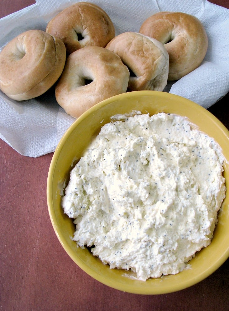 Photo of Easy Everything Bagel Dip a white creamy dip in a yellow bowl next to a basket of bagels on a brown table 