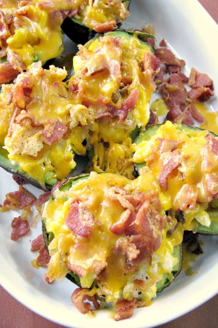 Close-up photo of baked avocados stuffed with eggs, potatoes, bacon and cheese in a white baking dish