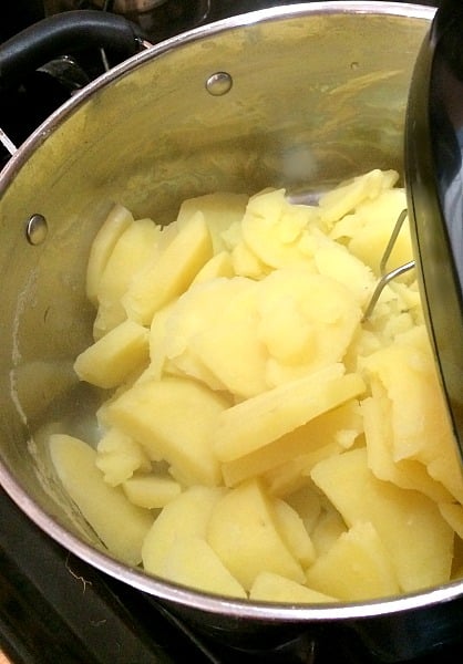 Photo of cooked potatoes in a pot about to be mixed with a hand mixer. 