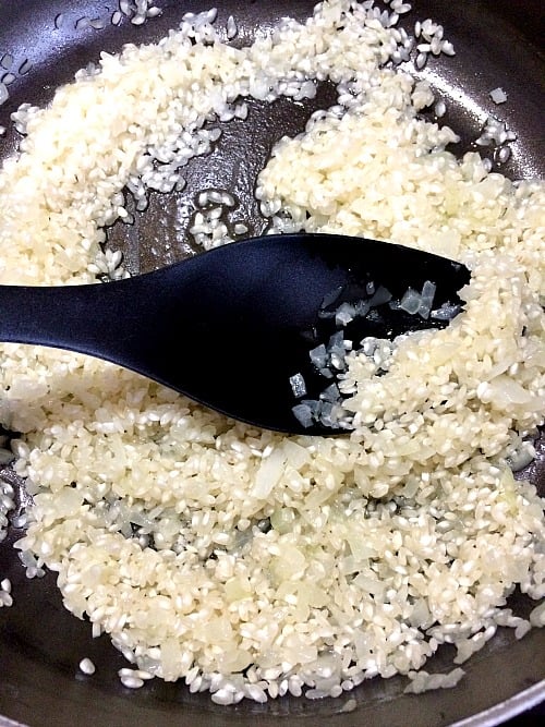 Photo of rice and onions sauteed in in olive oil and butter with a black spoon in the pan
