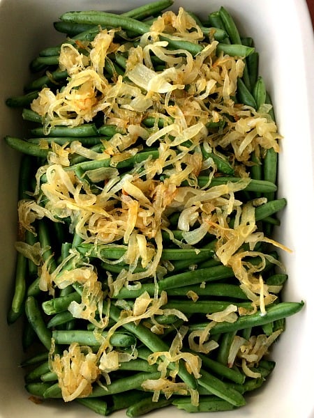 Photo of green beans in a white baking dish topped with caramelized onions 