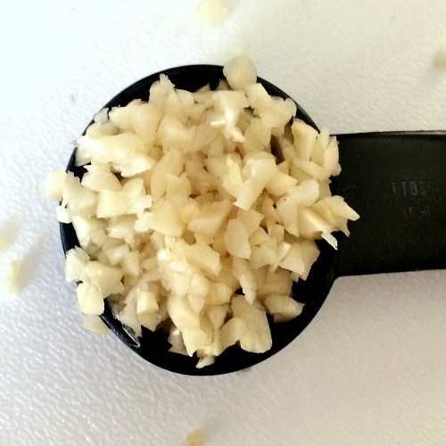Photo of a measuring tablespoon of minced garlic on a white cutting board 