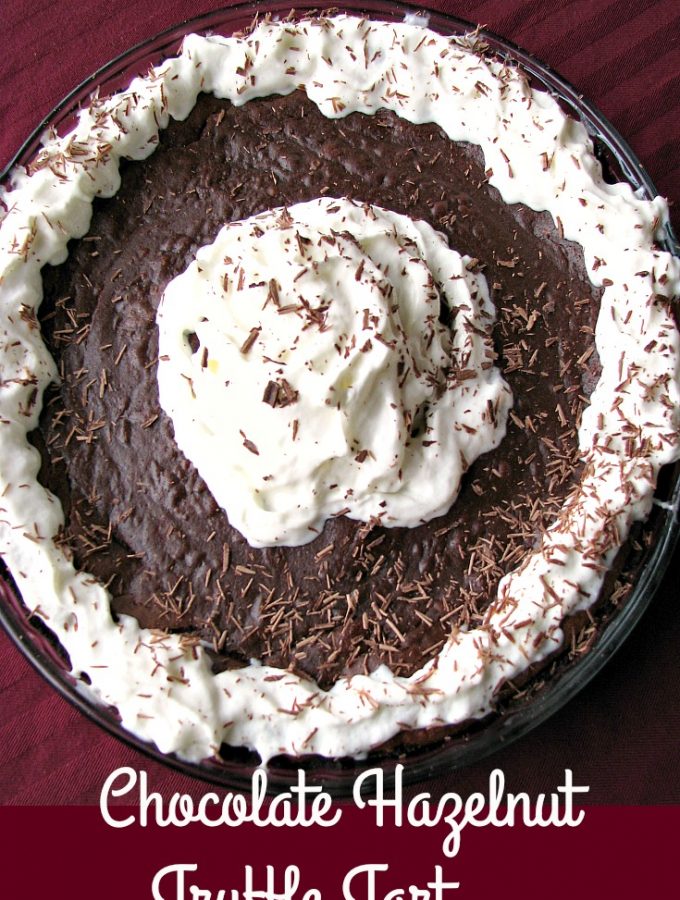 Photo of a whole Chocolate Hazelnut Truffle Tart topped with whipped cream and shaved chocolate
