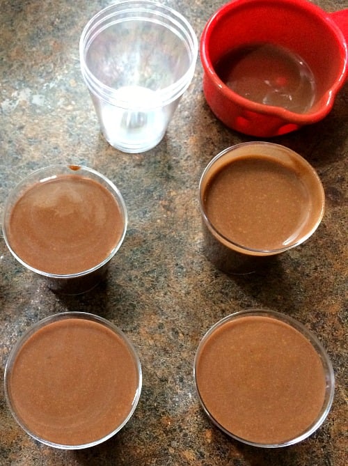 Photo of chocolate eggnog pudding shots in shot glasses next to a red measuring cup
