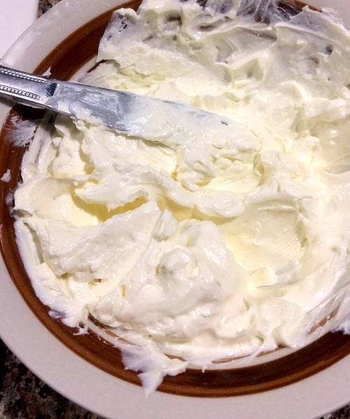 Photo of softened cream cheese in a bowl with a butter knife on the left-hand side 