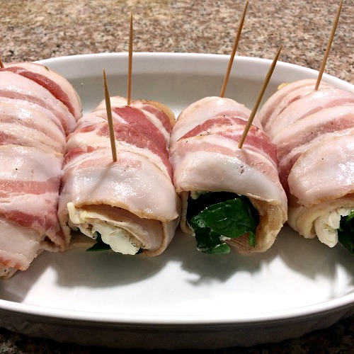 Photo of bacon wrapped stuffed chicken breasts in a white baking dish 