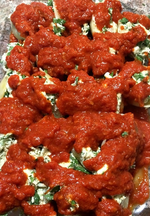 Photo of stuffed shells topped with pasta sauce in a glass baking dish