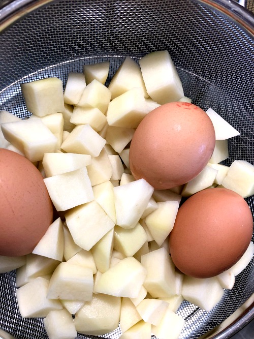 photo of diced potatoes and whole eggs in a mesh colander 