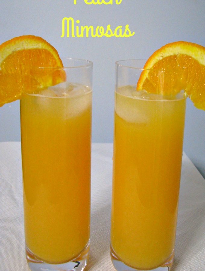 Front facing photo of two glasses of peach mimosas with orange slices on the rims