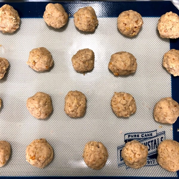 Photo of rolled walnut crumb cookies on a baking sheet lined with a baking mat 