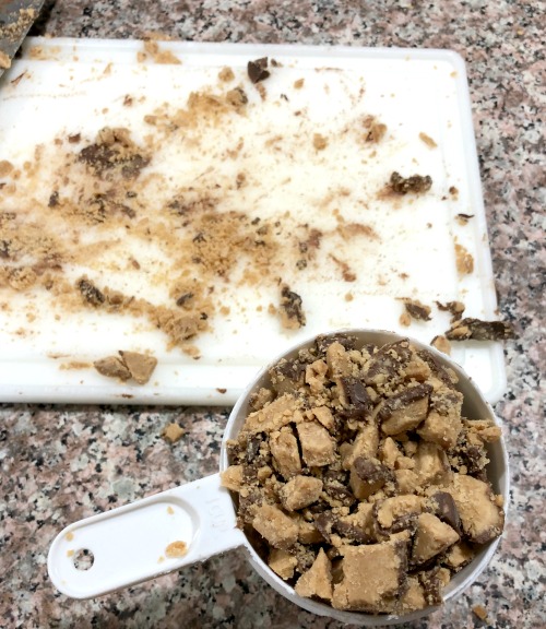 photo of chopped chopped peanut butter cups in a measuring cup next to a white cutting board with chopped chocolate peanut butter on it