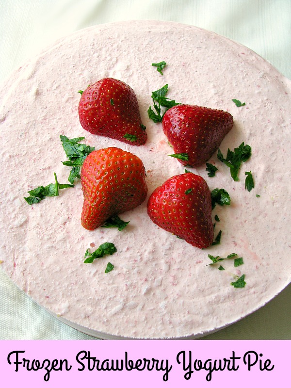 photo of Frozen Strawberry Yogurt Pie garnished with whole strawberry and minced parsley on a white tablecloth.
