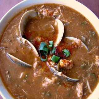 photo of seafood gumbo with whole clams on top in a white bowl