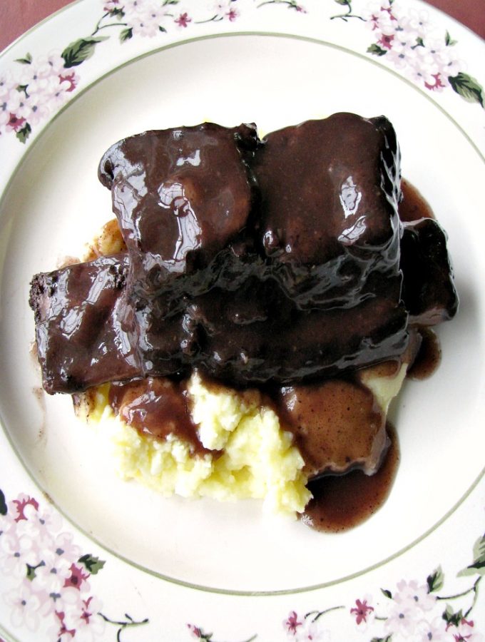 photo of plated Slow Cooker Red Wine Braised Short Ribs over mashed potatoes on a white flower trimmed plate