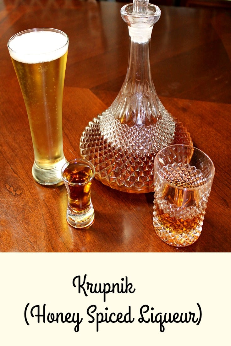 photo of a shot glass of Krupnik (honey spiced liqueur) in a shot glass next to a glass of beer a bottle and a glass on a wood table 