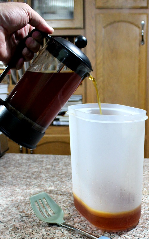photo of tea and spices being poured into a large beverage pitcher 