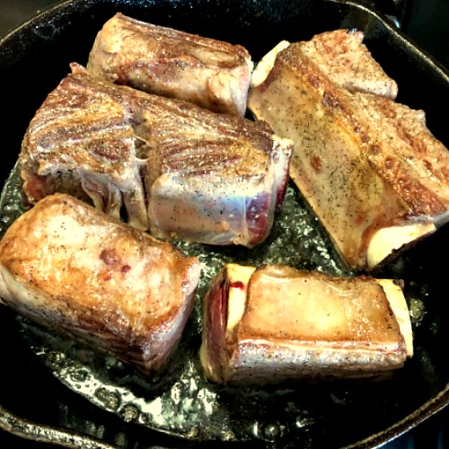 photo of short ribs browning in a cast iron pan