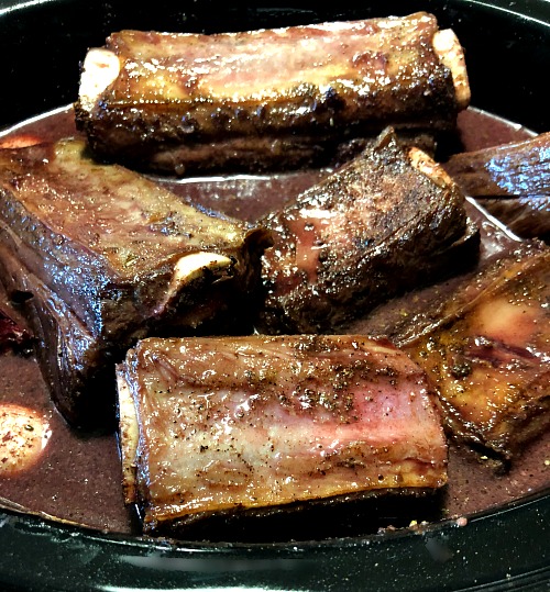 photo of short ribs with red wine beef broth and seasonings in a black slow cooker
