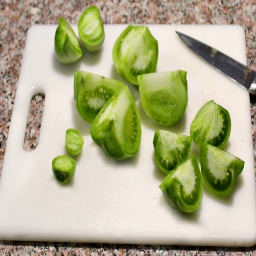 photo of sliced green tomatoes on a white cutting board with a knife on the right side 