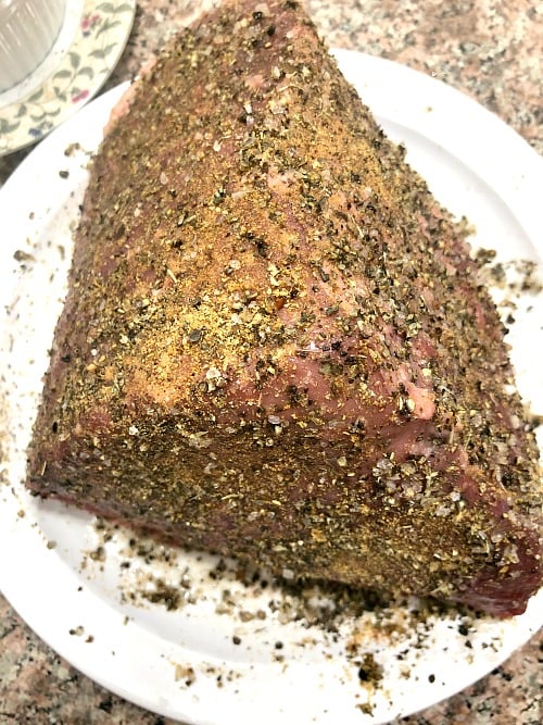 Photo of top round beef coated with olive oil and seasonings on a plate 