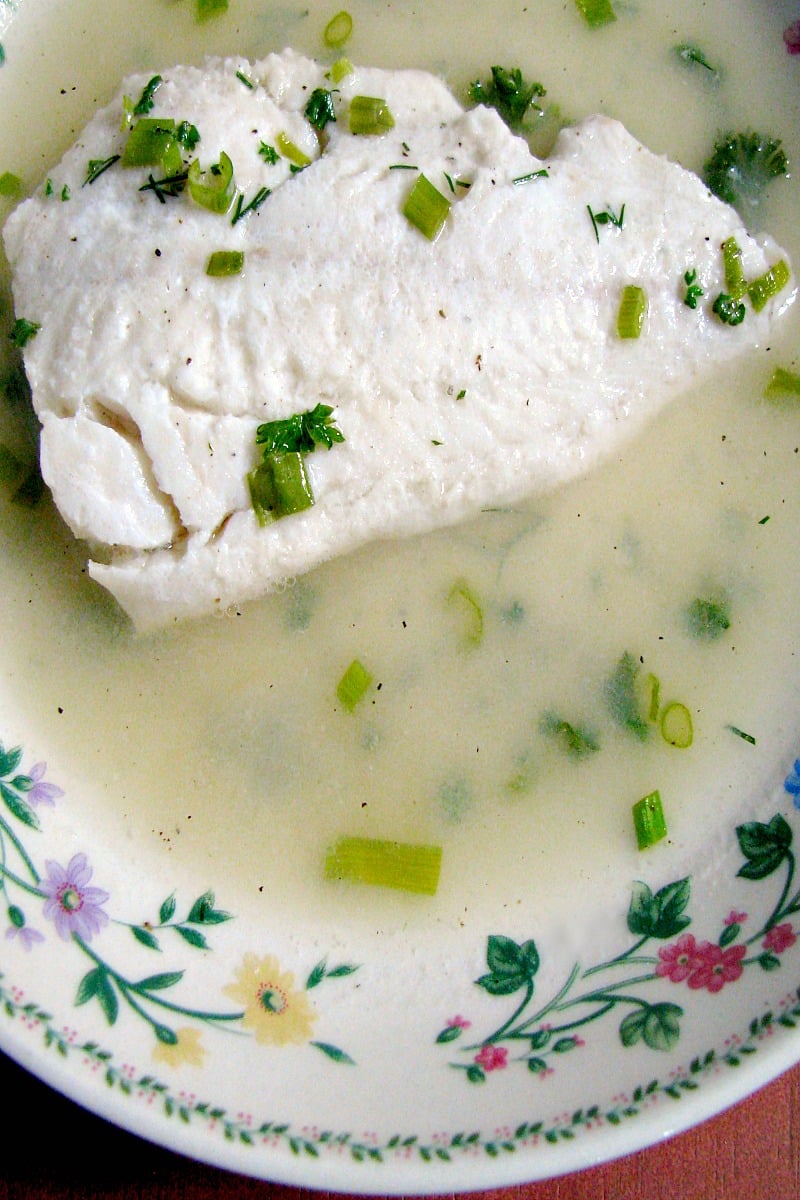 Close up photo of a shallow bowl with poached haddock in herbed broth 