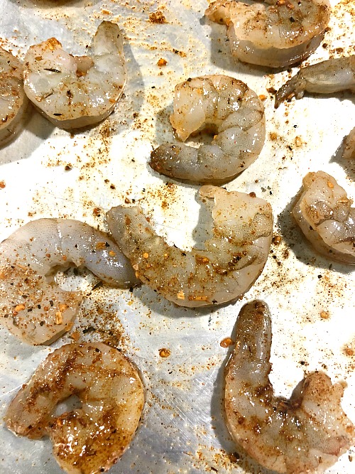 photo of raw shrimp tossed with cajun seasoning on a baking sheet 